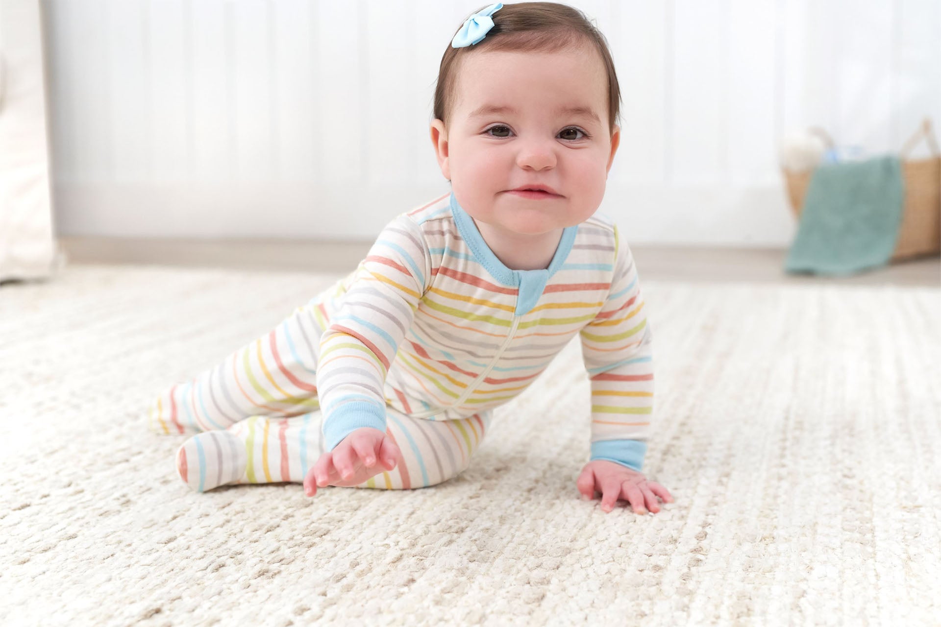 Adorable baby girl lying on white bedding, wearing a pink Gerber Childrenswear footed sleeper covered in colorful ice cream cone prints. This cozy baby sleeper features soft, breathable fabric perfect for restful sleep or nap time. Shop Gerber Childrenswear for affordable baby pajamas, newborn sleepers, and toddler sleepwear deals.